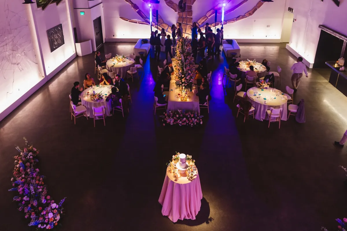 Overhead view of a wedding reception with purple uplighting, round tables and a pink-draped cake table