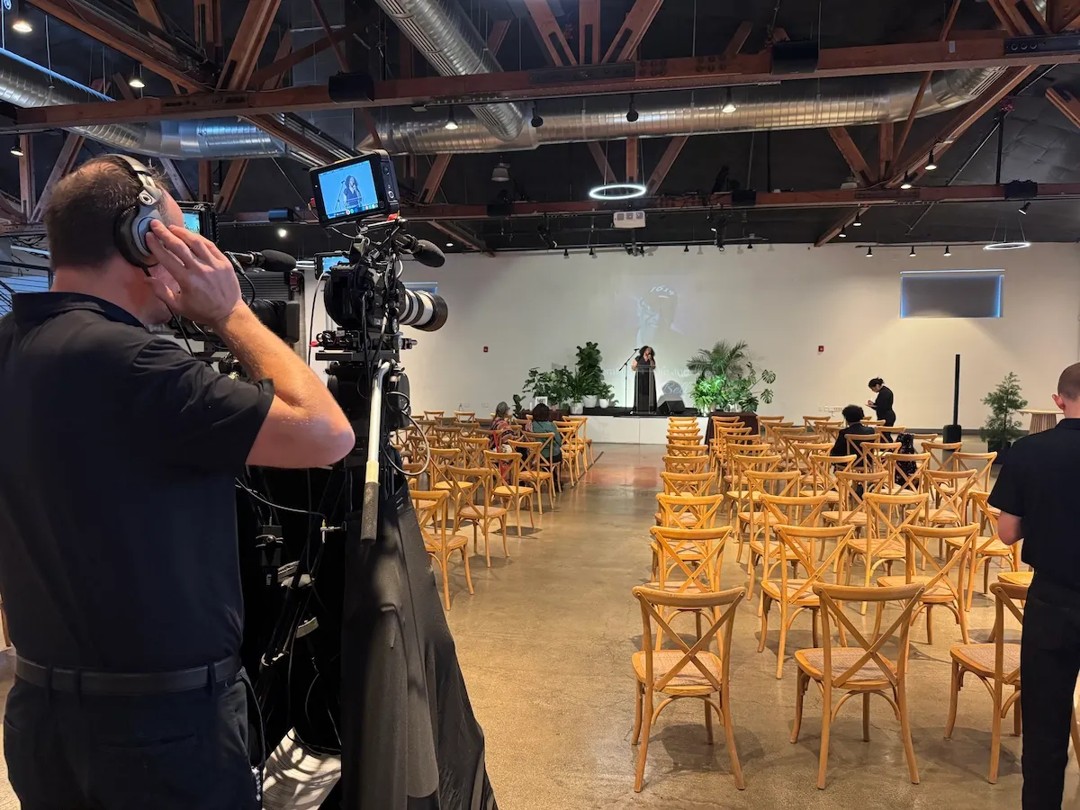 Camera operator filming a ceremony setup with rows of wooden chairs for a livestream