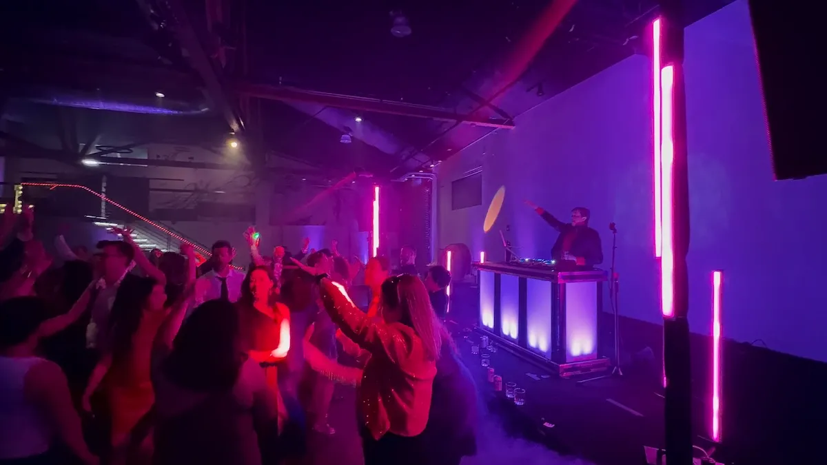 Crowd dancing with hands in the air under purple light and LED columns