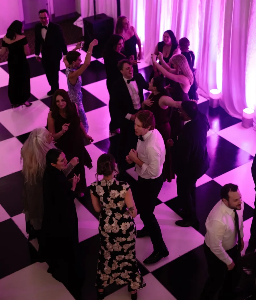 Wedding guests dancing on a black-and-white checkered floor under pink uplighting