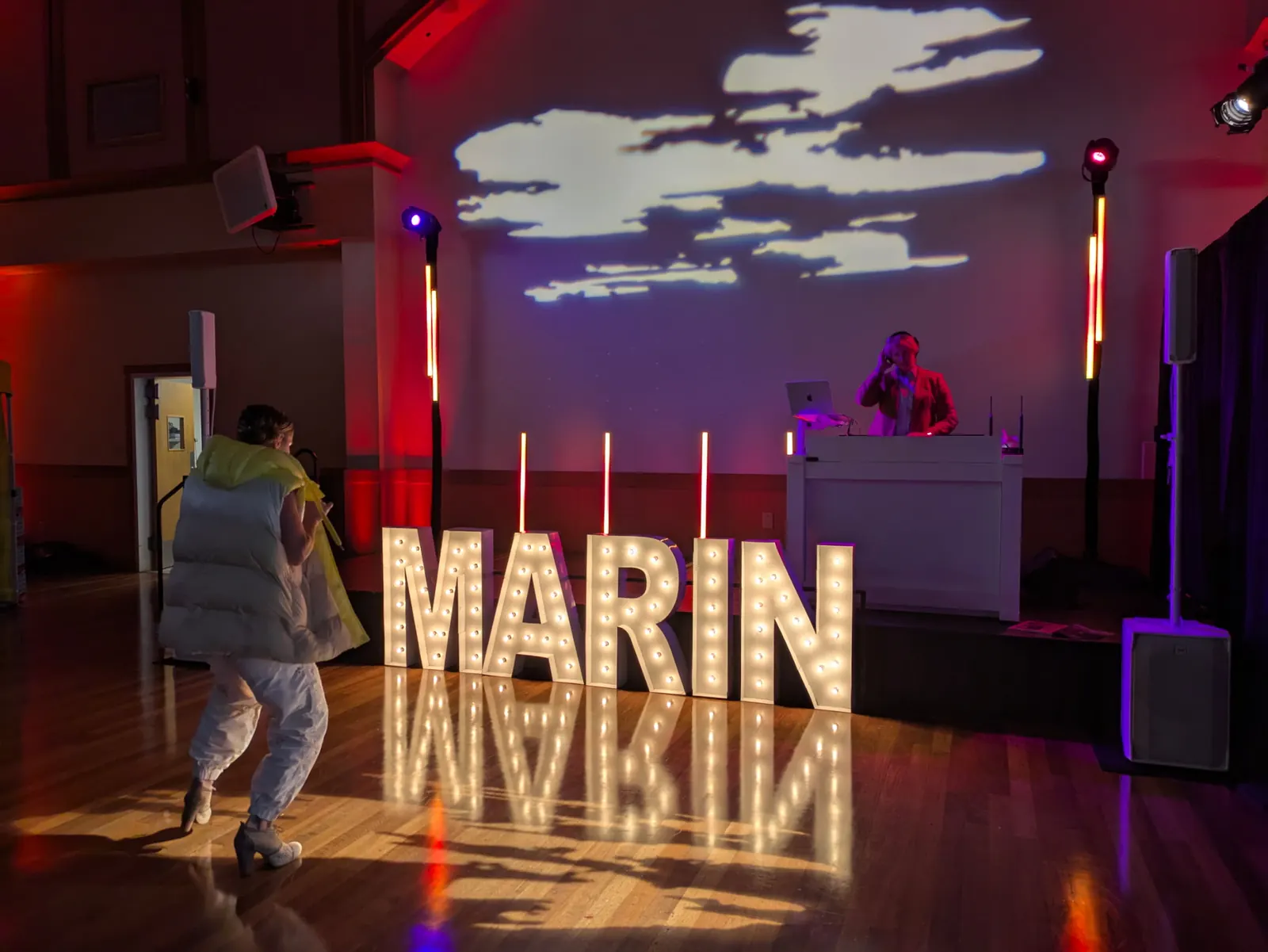 Light-up MARIN marquee letters on the dance floor with a DJ booth and cloud projections behind
