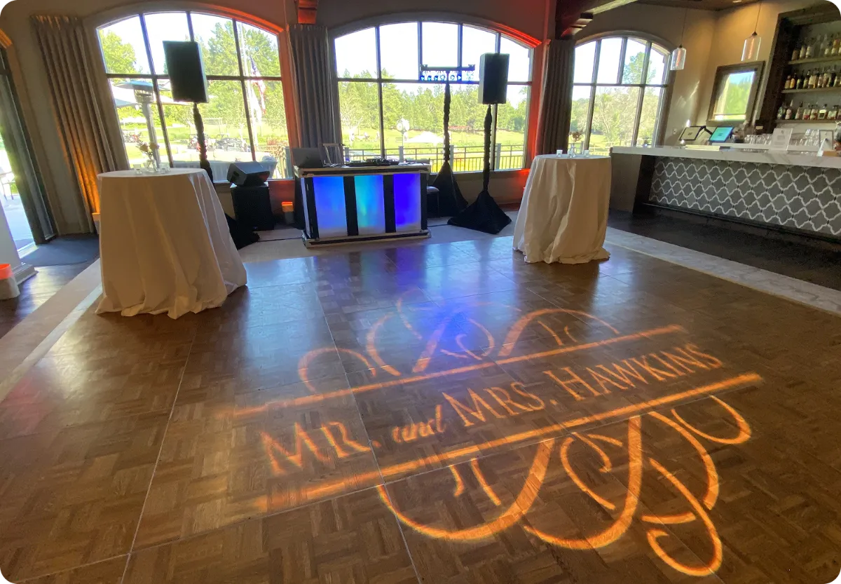 Custom wedding monogram projected onto a wooden dance floor with warm uplighting