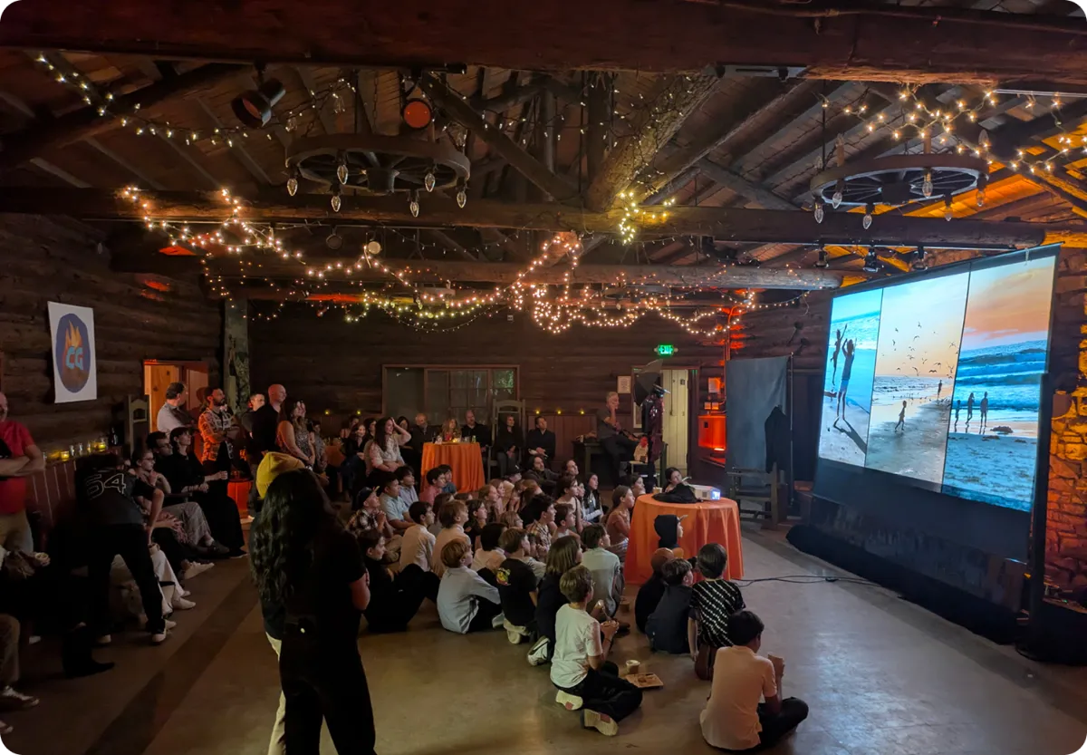 Guests watching a large screen in a rustic venue with string lights
