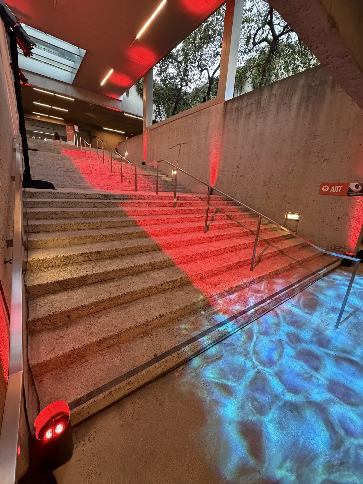 Staircase washed in red light with a blue water-ripple effect on the landing