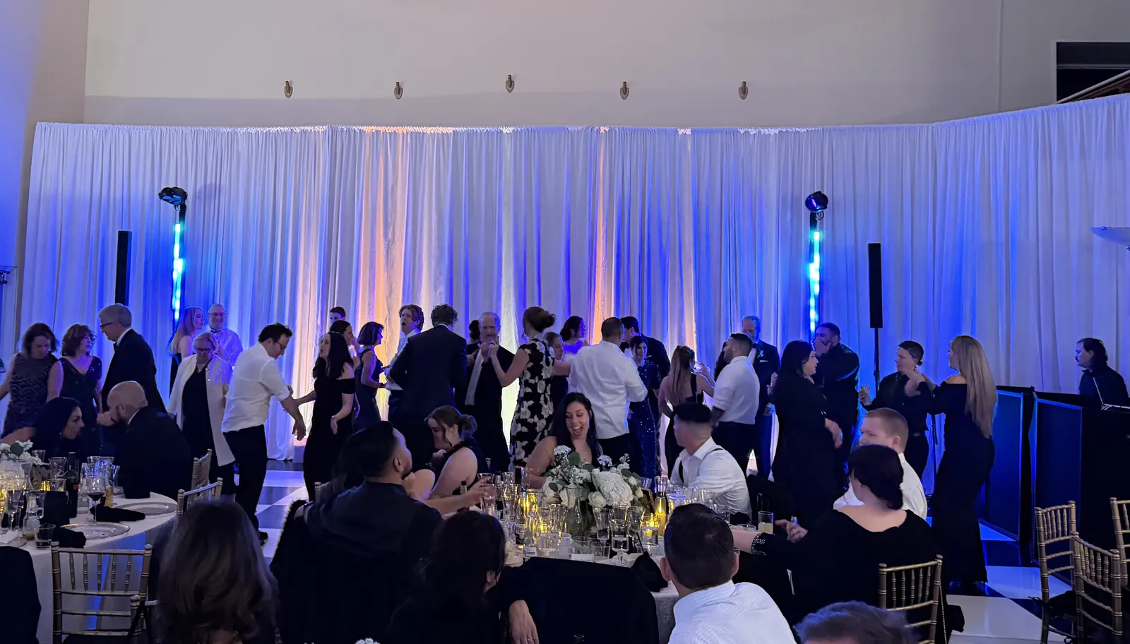 Wedding guests dancing between white drapes washed in blue uplighting