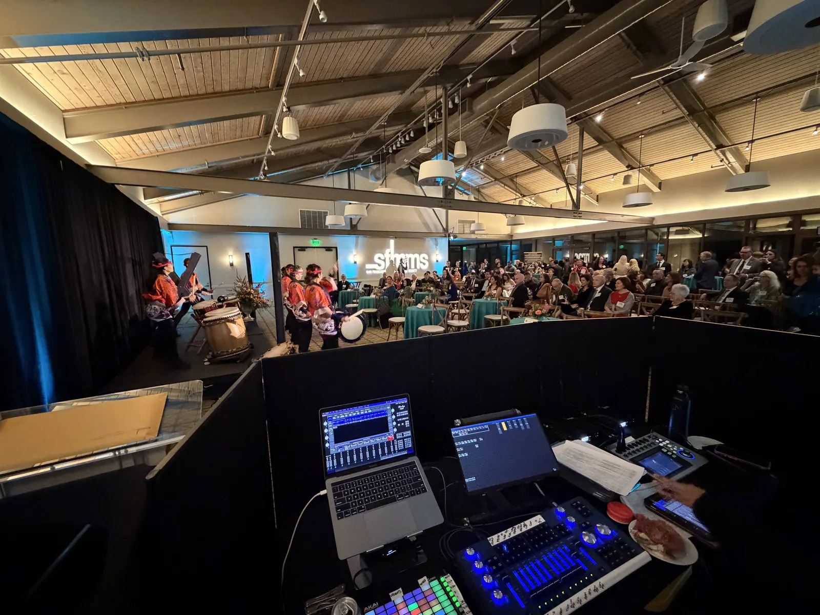 Corporate event seen from the AV booth, with a mixing console and laptops in the foreground