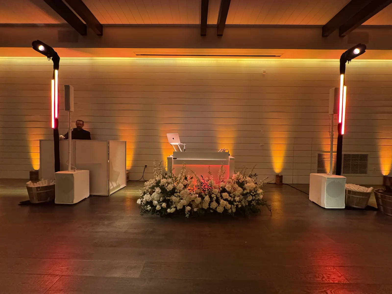 White DJ booth with flowers and amber uplighting along white wood-paneled walls