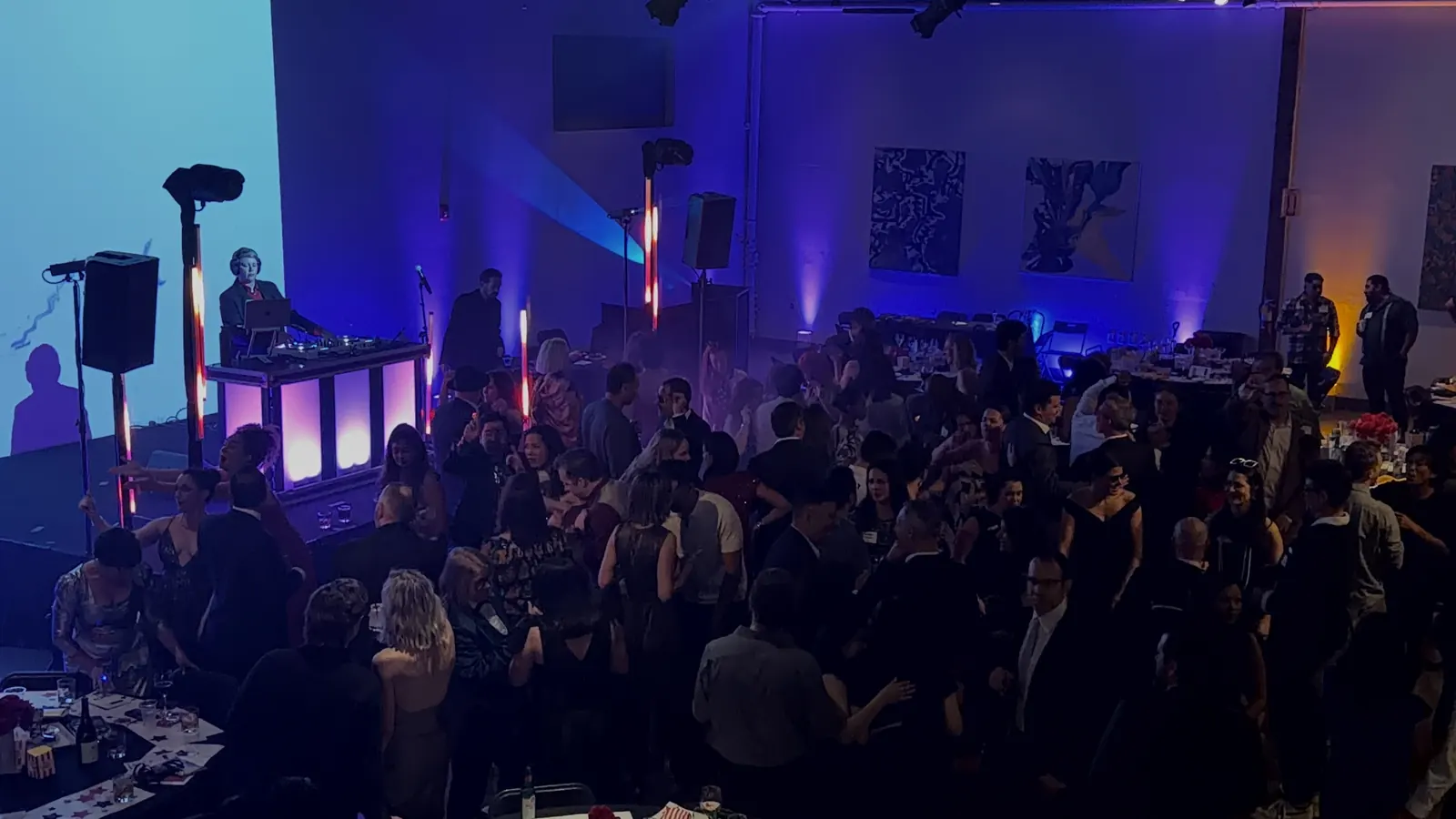 Party crowd under purple and blue lighting with a lit DJ booth