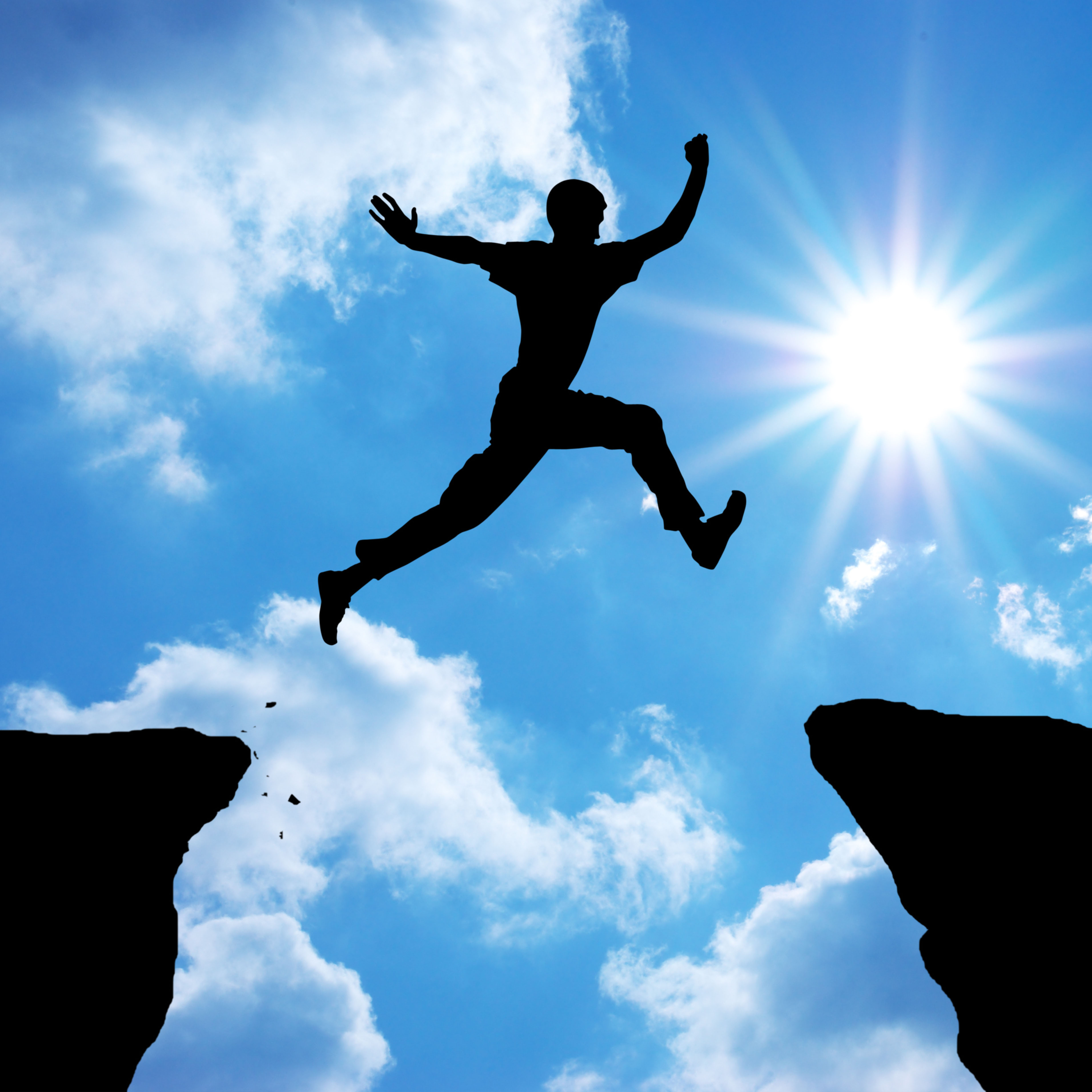 A person leaping across a gap between two cliffs toward the sun
