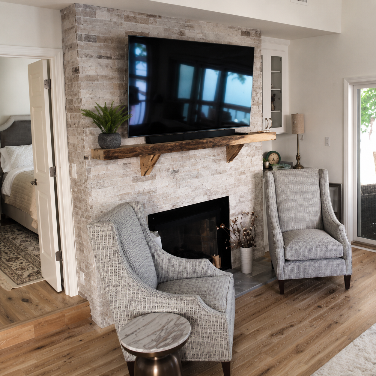 Light stacked stone fireplace surround with a natural wood mantel, mounted television, black firebox, and adjacent sitting area in Davidson, NC.