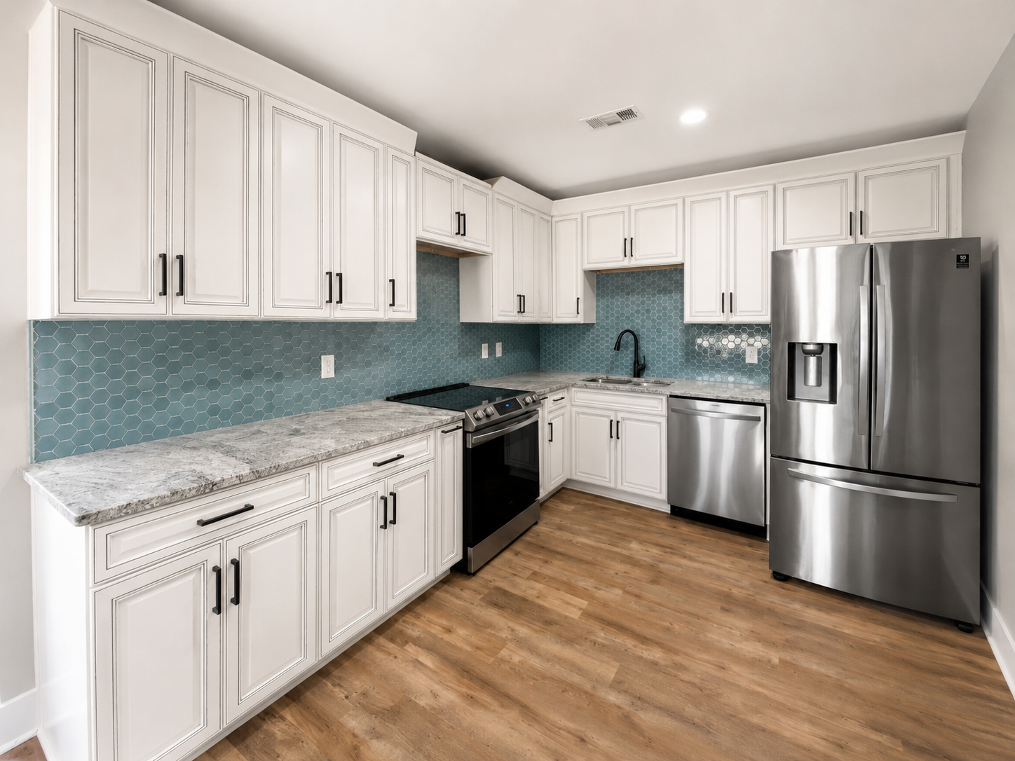 Blue hexagon tile backsplash installed between white kitchen cabinets and light stone countertops.