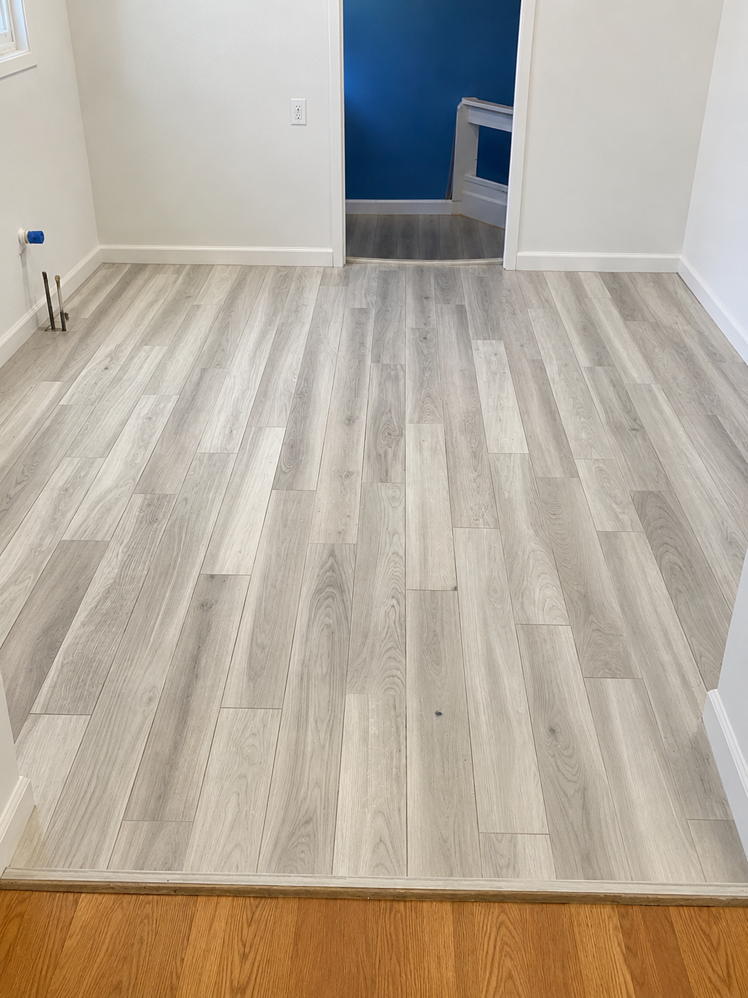 Light wood-look plank flooring installed across an empty interior room with a transition to existing hardwood flooring in Charlotte, NC