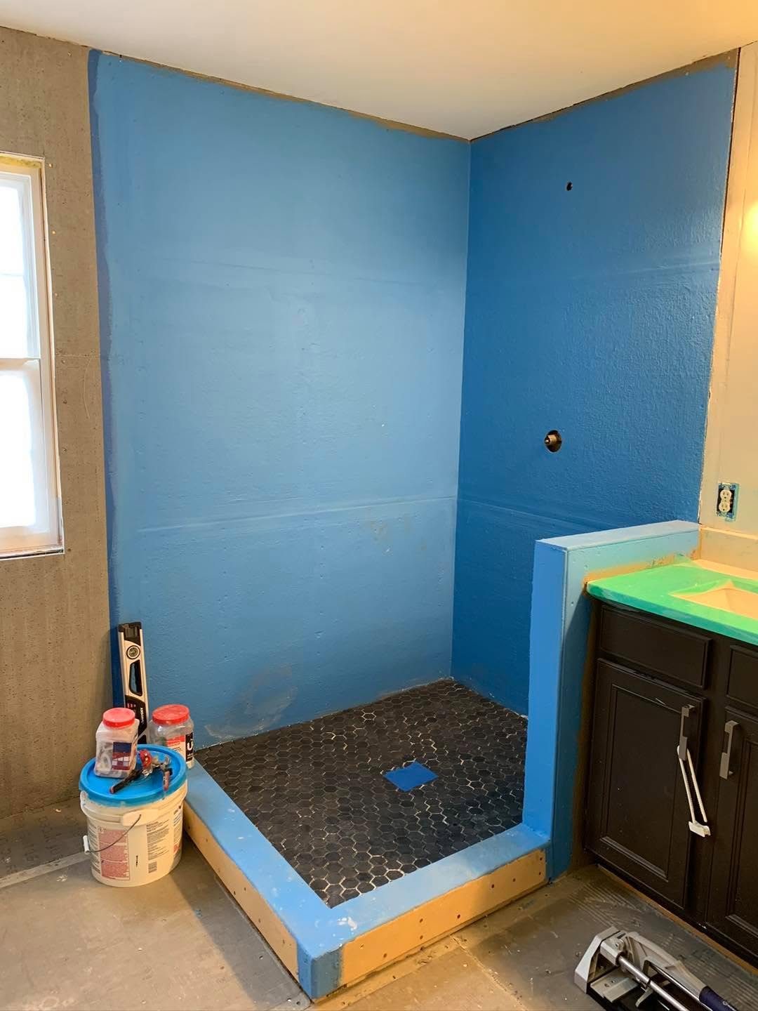 Bathroom shower under construction with blue waterproofing membrane, a raised curb, and dark hexagon mosaic floor tile in Fort Mill, SC