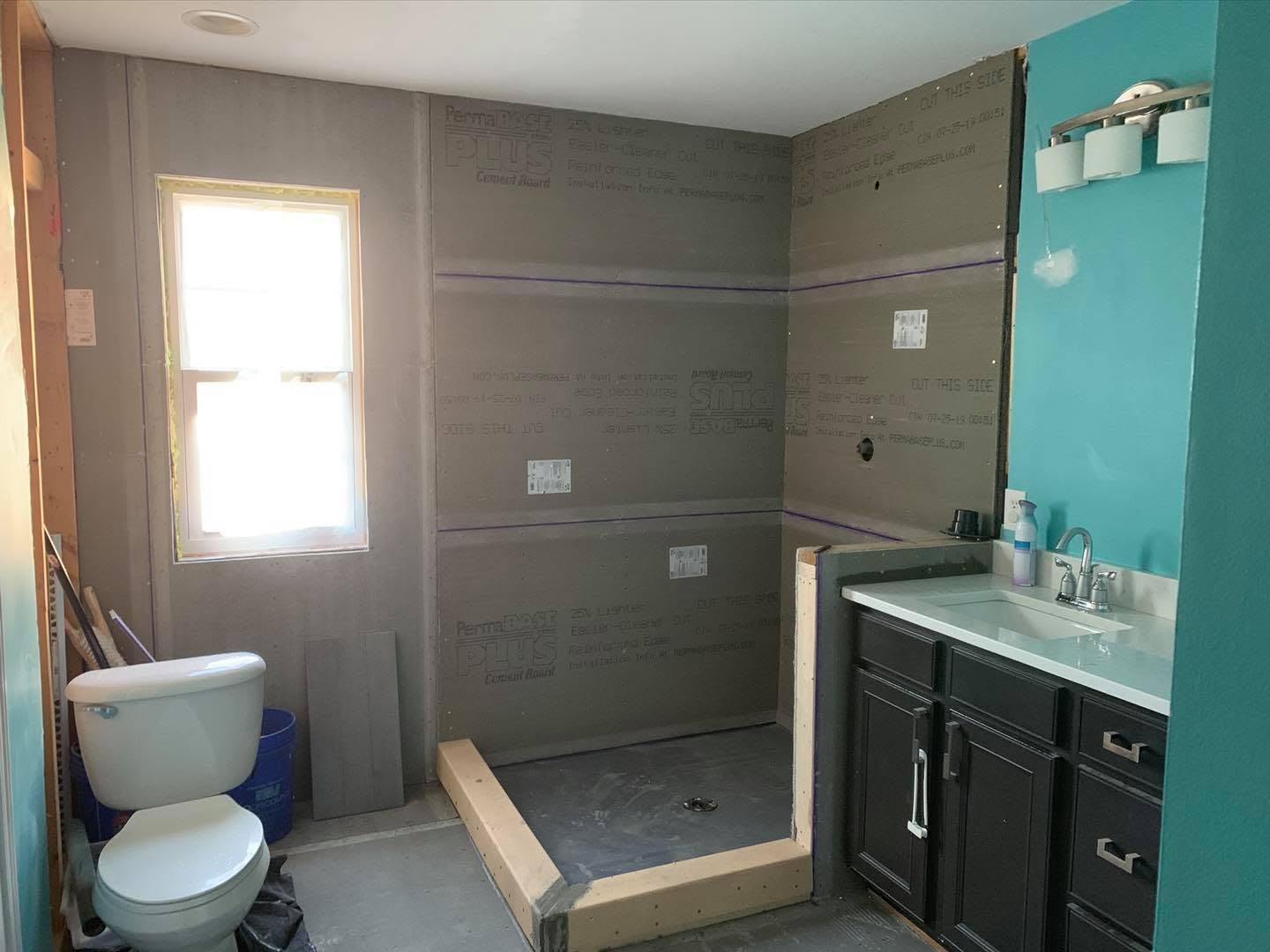 Bathroom shower under construction with cement backer board, framed curb, vanity, and exposed plumbing connections n Fort Mill, SC