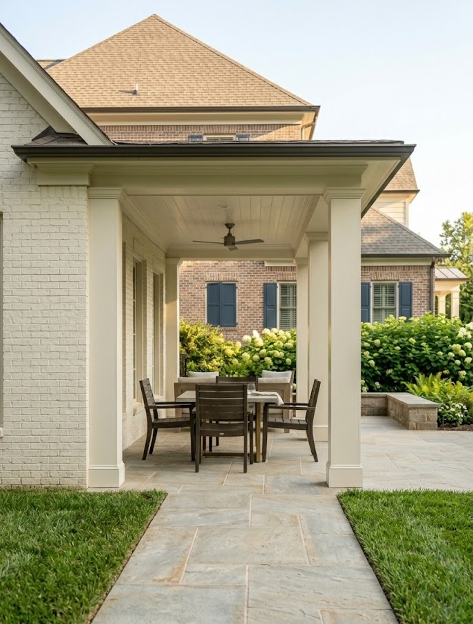 Front-facing view of a covered backyard patio with stone paving, white columns, outdoor dining furniture, and landscaped seat walls in Cornelius, NC.