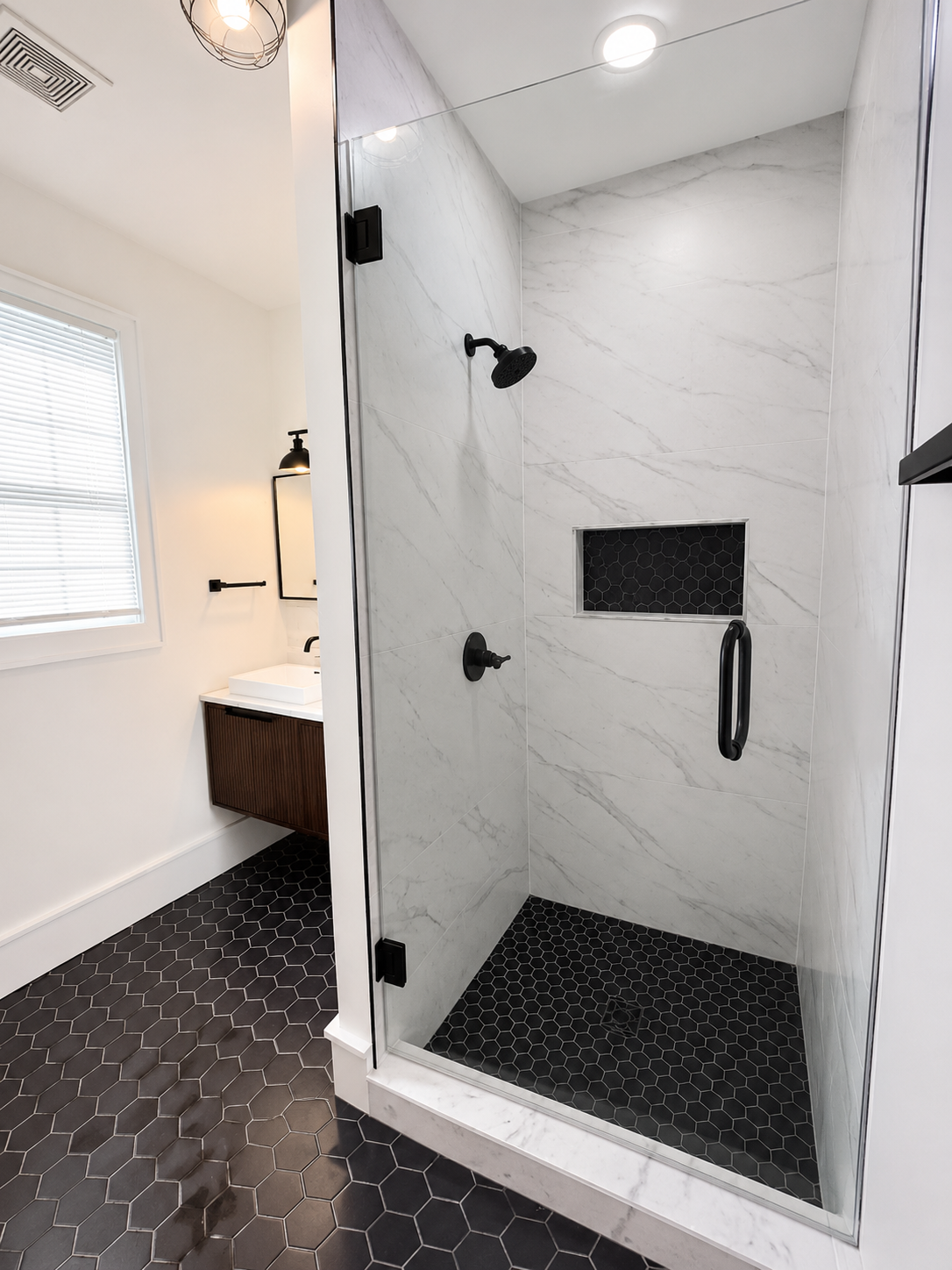 Frameless glass shower with large-format white marble-look wall tile, a black hexagon niche, black hexagon floor, and matte black fixtures in Concord, NC.