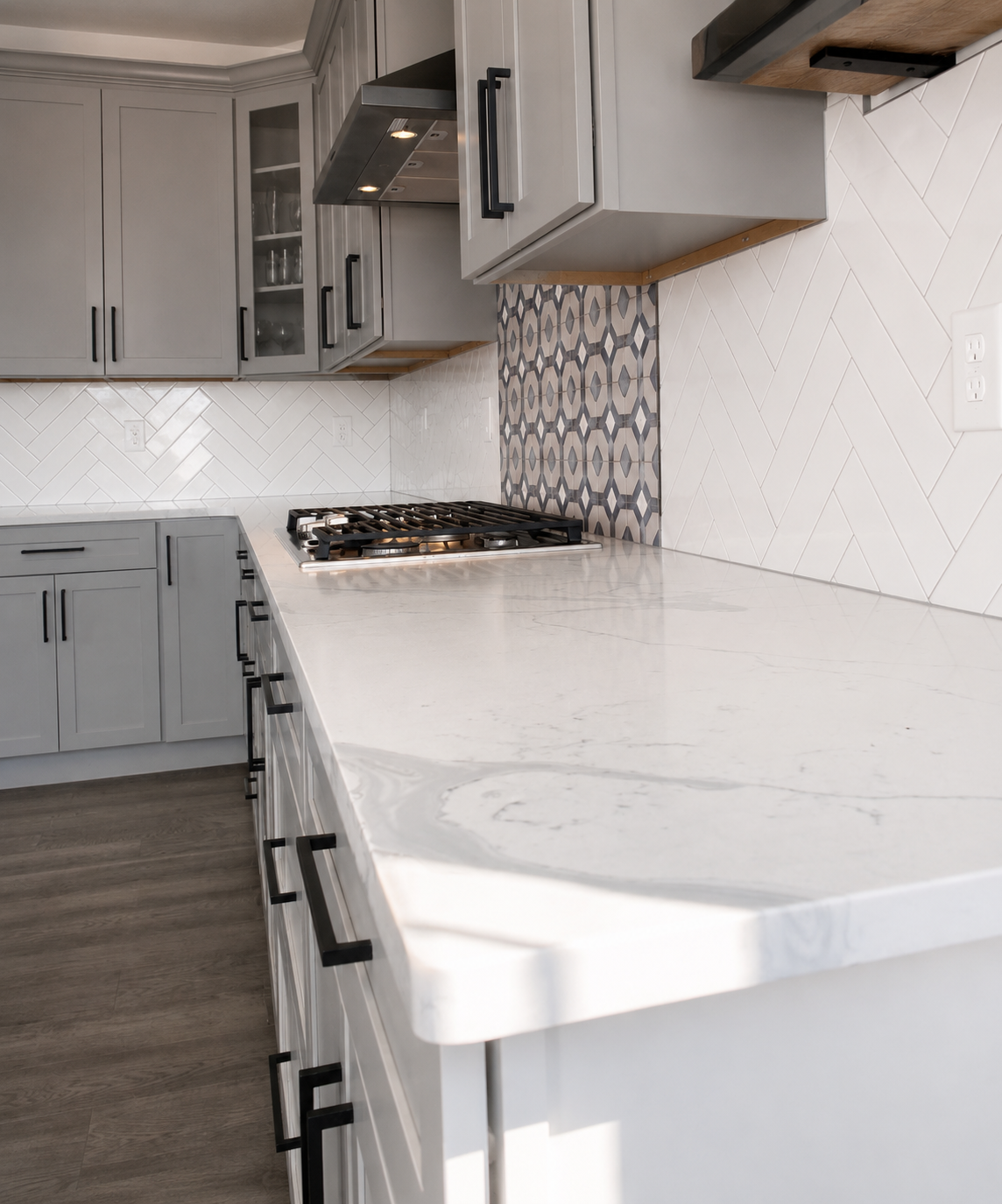 Angled view of a white herringbone tile kitchen backsplash with a gray geometric range feature, gray cabinetry, and white countertops in Mooresville, NC