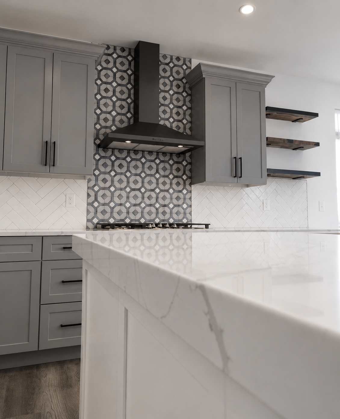 Gray and white geometric tile installed from the cooktop to the ceiling behind a black range hood, bordered by a white herringbone backsplash in Mooresville, NC