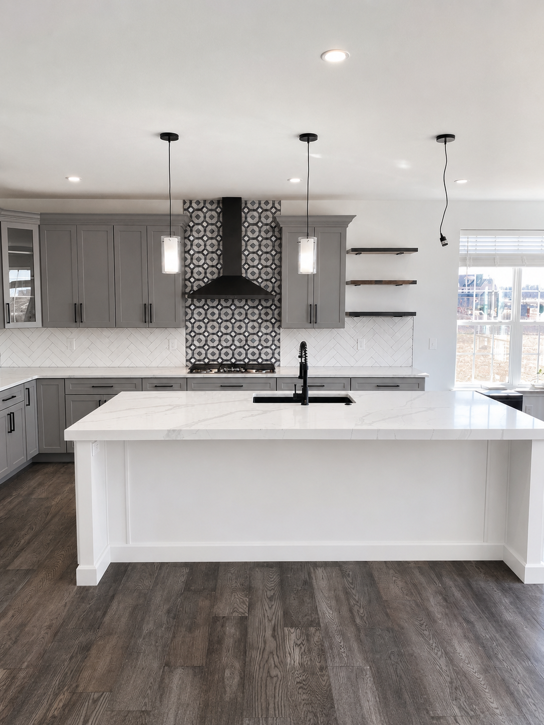 Wide kitchen with gray cabinets, a white island, white herringbone backsplash, geometric range tile, and black fixtures in Mooresville, NC.