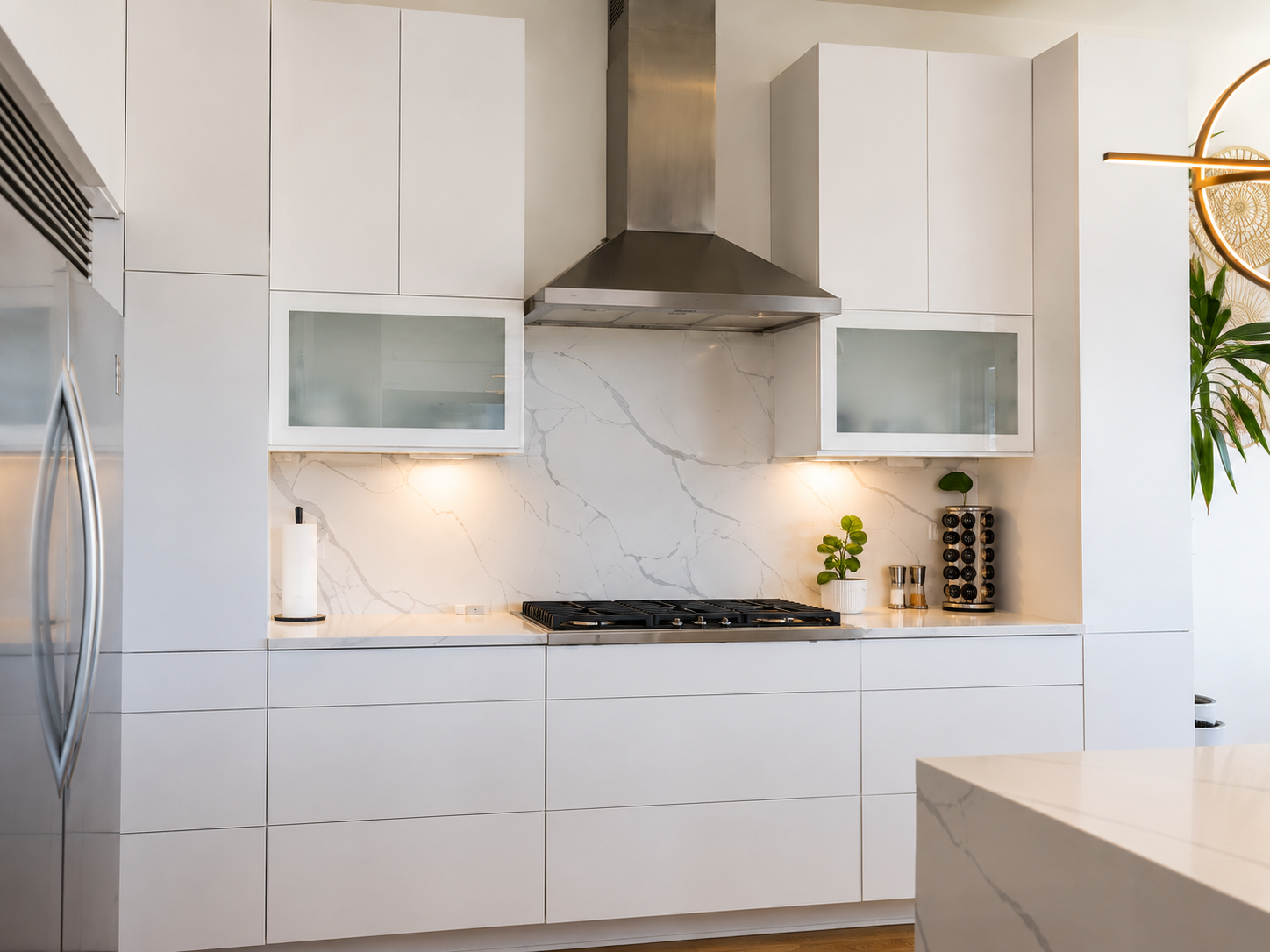 White marble-look slab backsplash installed behind a stainless steel range hood and cooktop between modern white cabinets in Charlotte, NC.