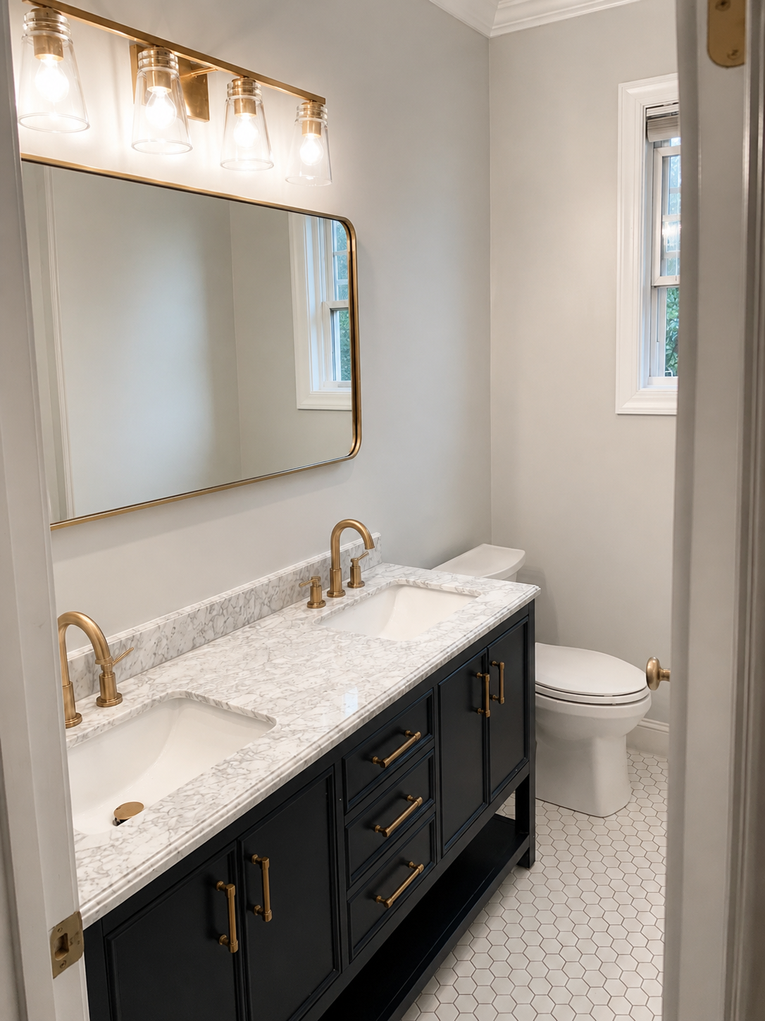 Angled bathroom view showing a black double vanity, brass fixtures, light stone countertop, and white hexagon tile floor in Waxhaw, NC