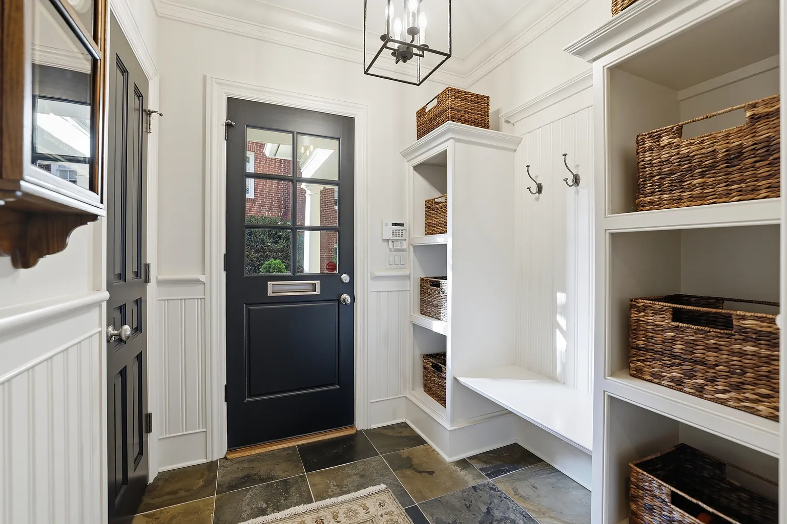 Traditional white mudroom with built-in storage, a bench, coat hooks, woven baskets, a dark entry door, and multicolored slate tile flooring in Huntersville, NC