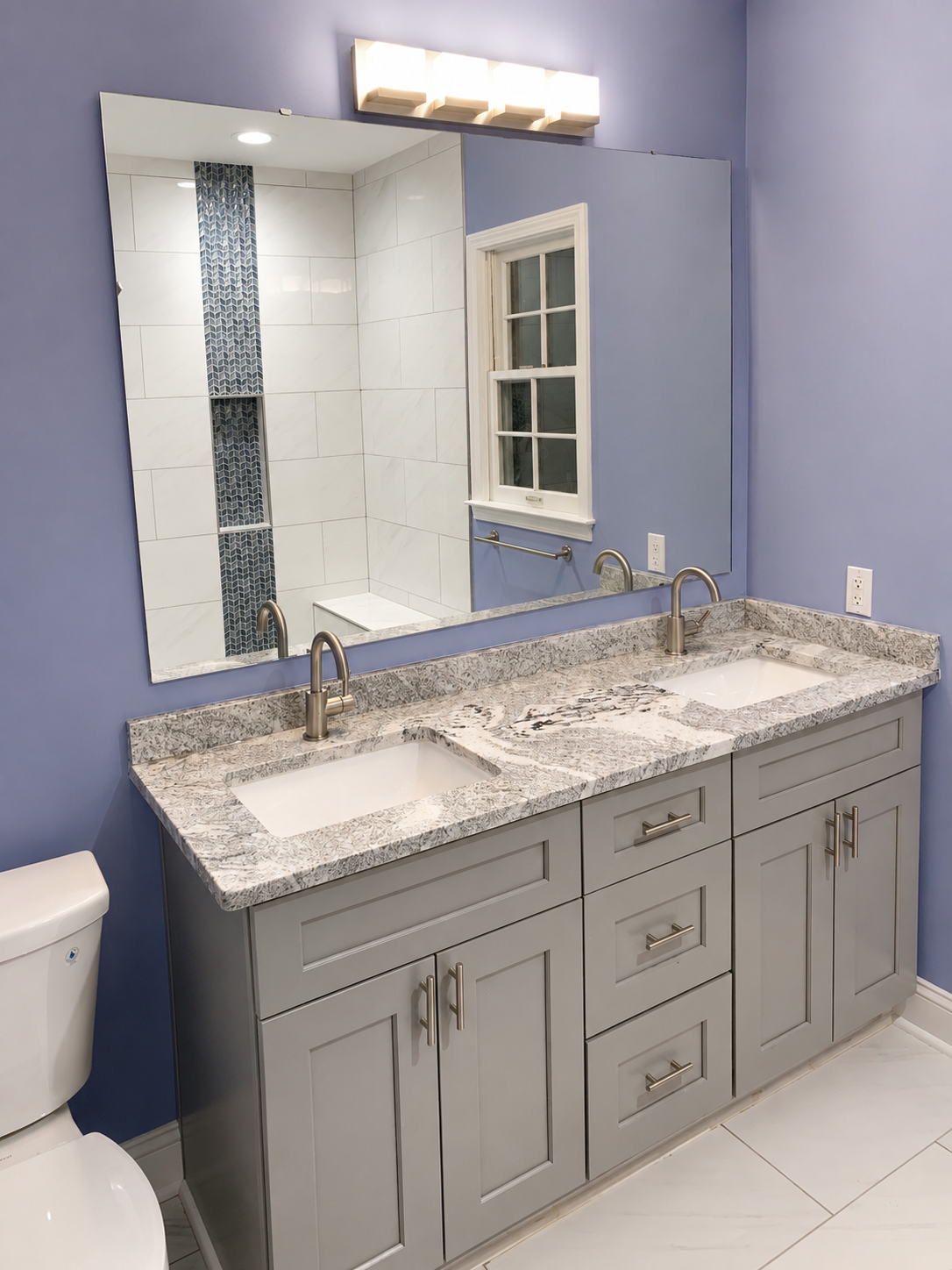 Bathroom with a gray double vanity, light stone countertop, large-format floor tile, and a shower reflected in the mirror with a vertical blue mosaic accent in Davidson, NC.