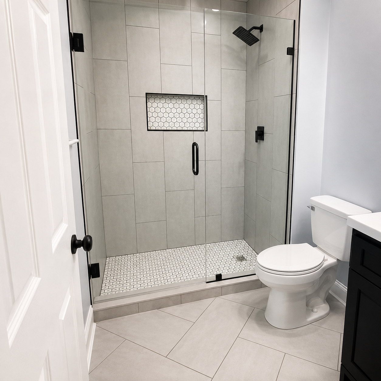 Frameless glass shower with large light gray wall tile, a white hexagon mosaic niche and floor, and matte black fixtures in Fort Mill, SC