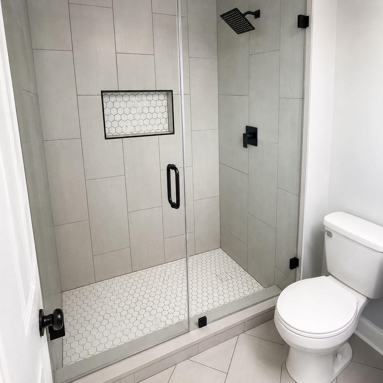 Closer view of a light gray tiled shower with a white hexagon mosaic niche, matching mosaic floor, clear glass enclosure, and black fixtures in Fort Mill, SC