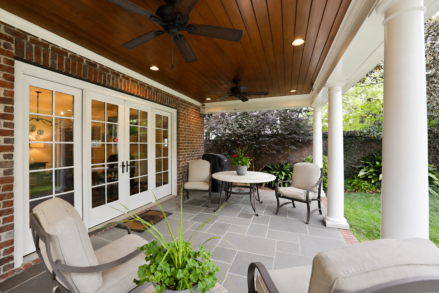 Covered backyard patio with gray rectangular stone flooring, white columns, a warm wood-plank ceiling, and views of the landscaped yard in Charlotte, NC
