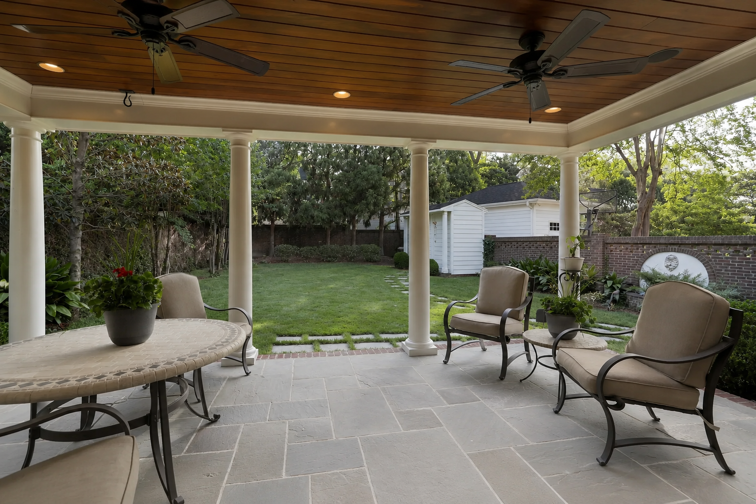 Reverse view of a covered brick patio with gray rectangular stone flooring, white French doors, white columns, and a wood-plank ceiling in Charlotte, NC