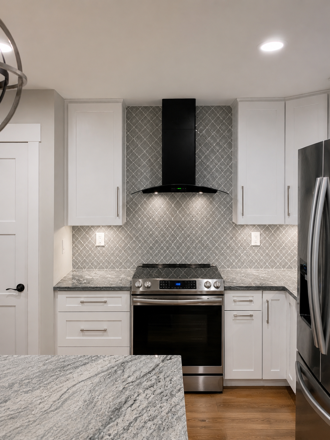 Finished kitchen with a gray arabesque mosaic backsplash installed from the countertop to the ceiling behind a black curved range hood in Davidson, NC