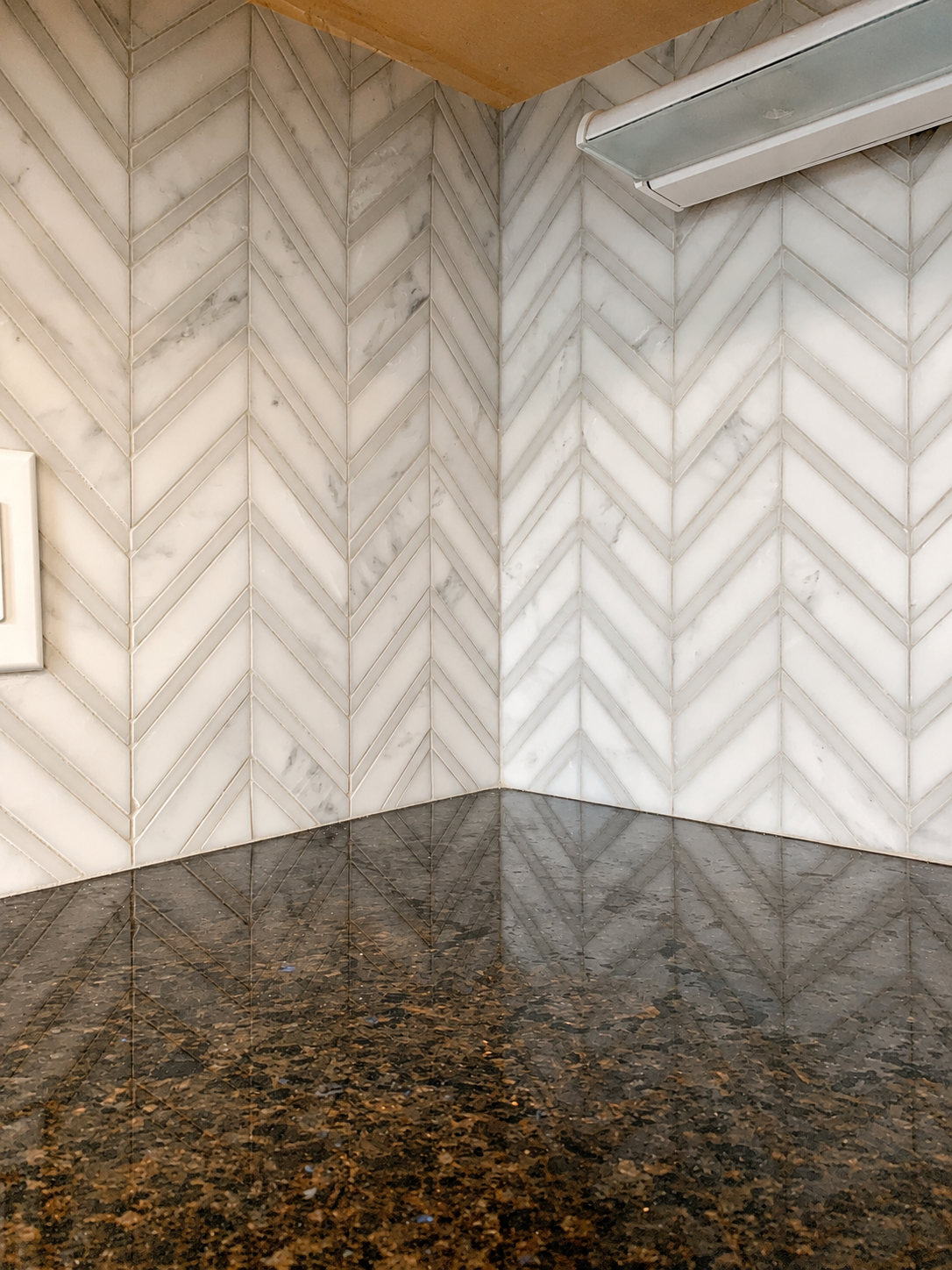 Close-up of a white marble chevron backsplash meeting precisely at an inside kitchen corner above a dark stone countertop in Charlotte, NC