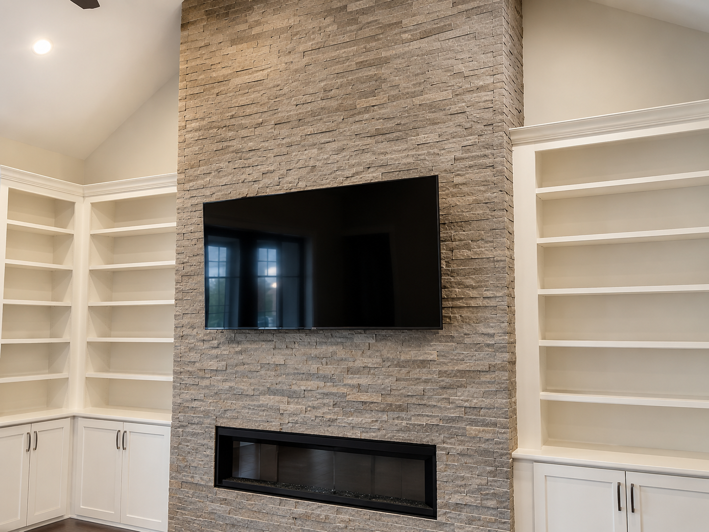 Floor-to-ceiling gray stacked-stone fireplace wall with a linear firebox, mounted television, and white built-in shelving in Mooresville, NC by Lake Norman.