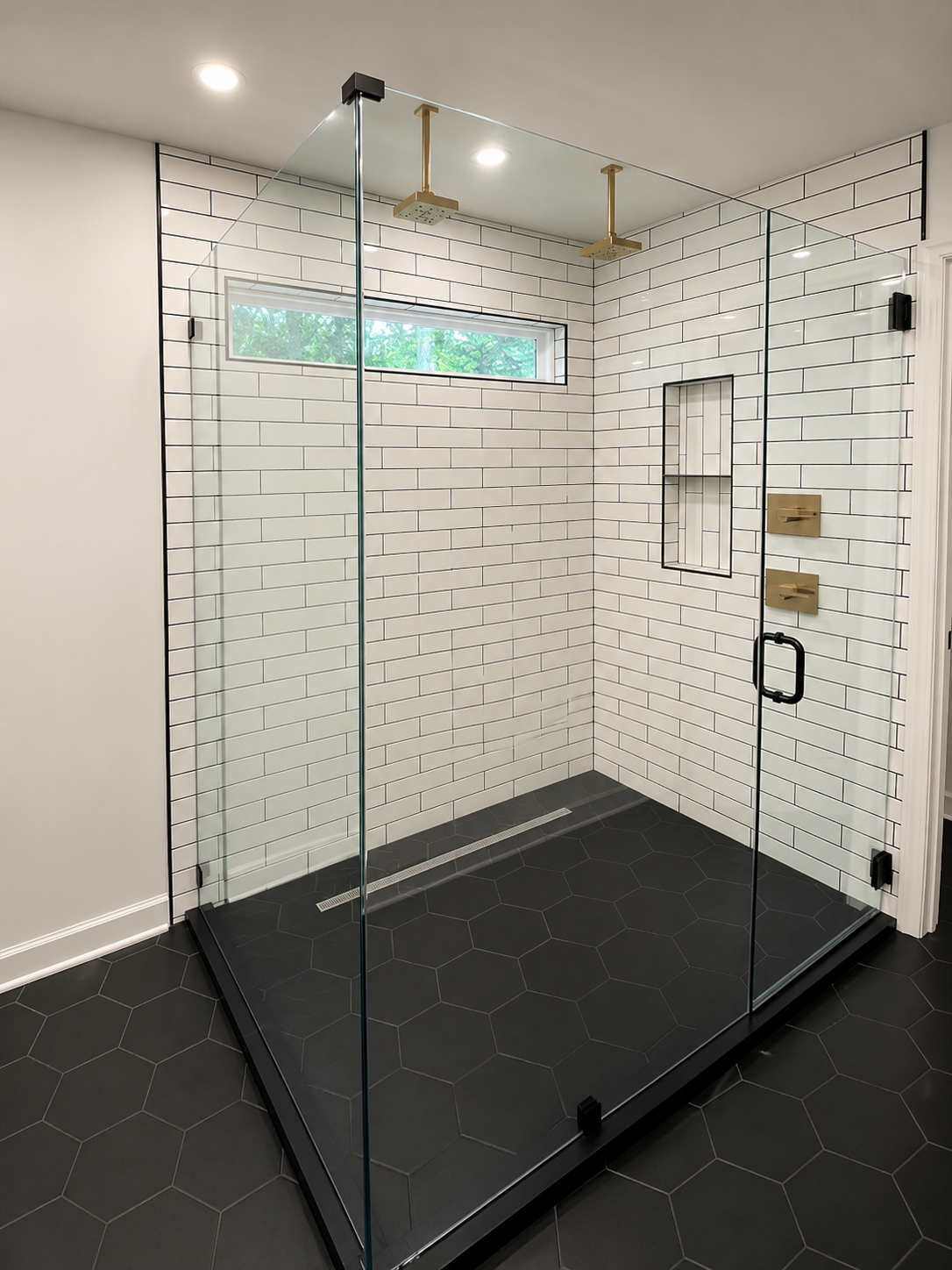 Large frameless walk-in shower with white subway wall tile, contrasting dark grout, black hexagon flooring, and brushed brass fixtures in Fort Mill, SC