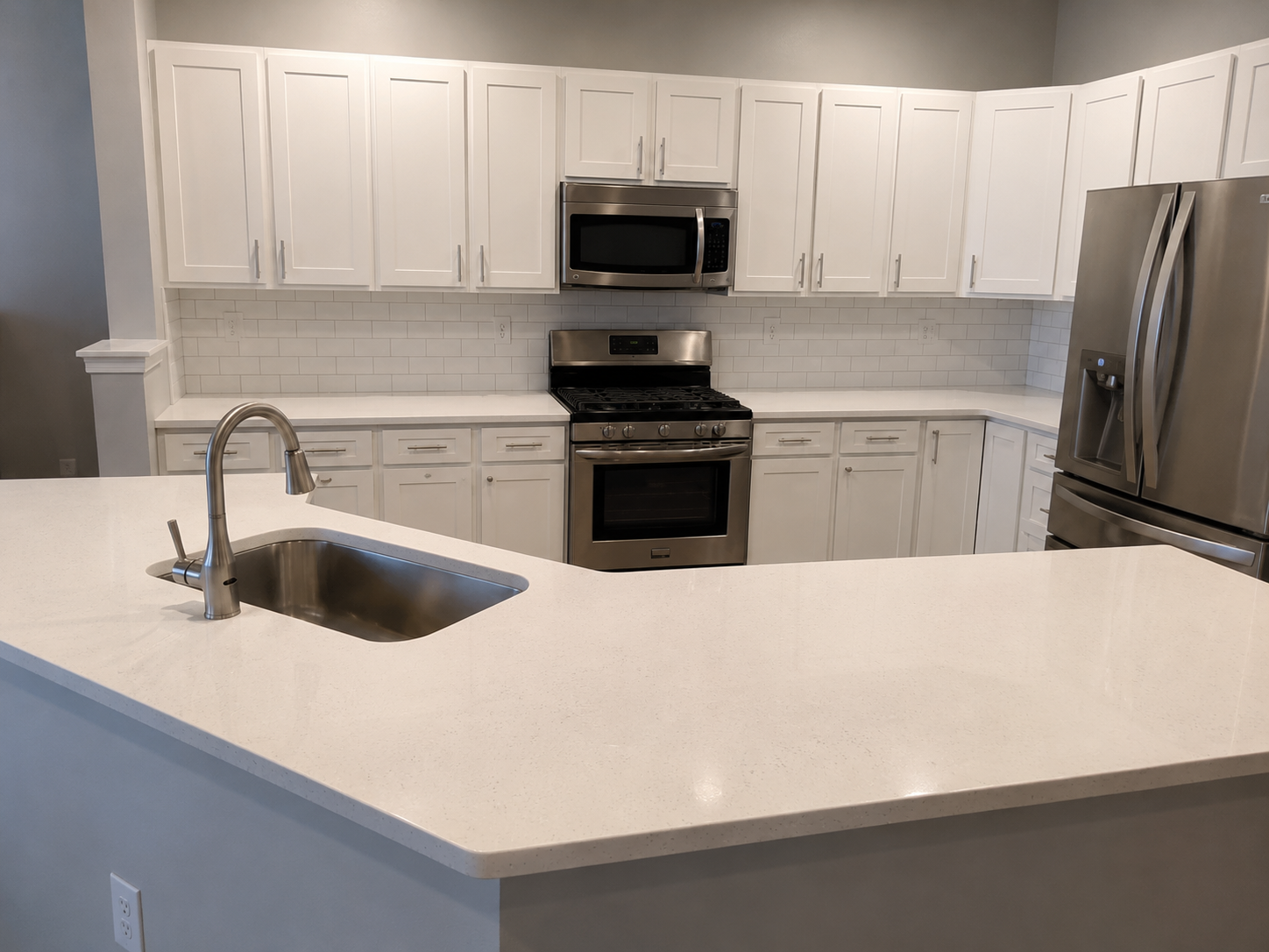 Bright white kitchen with a horizontal subway tile backsplash, shaker cabinets, quartz countertops, stainless appliances, and a large peninsula in Harrisburg, NC