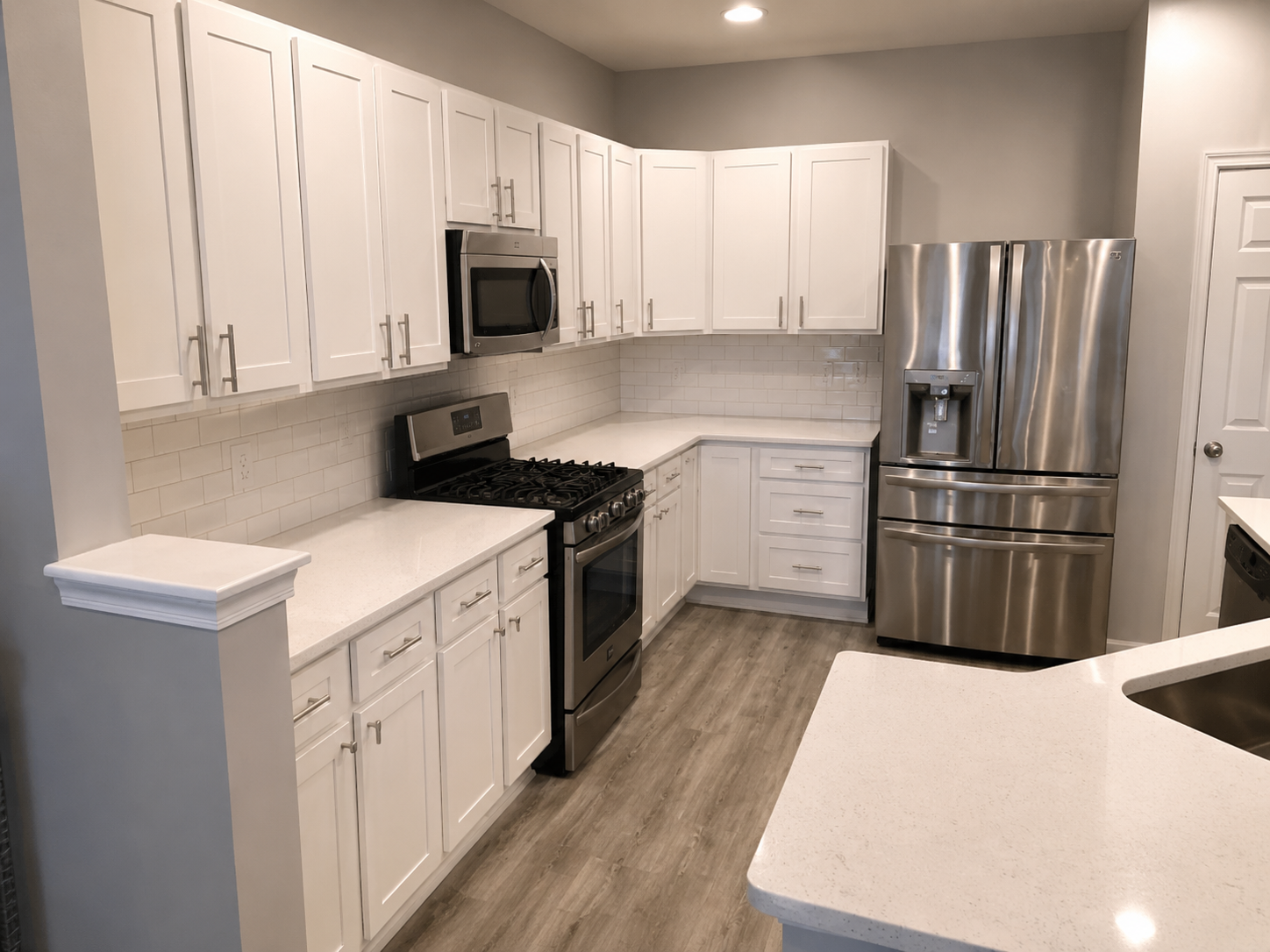 Completed white kitchen with shaker cabinetry, subway tile backsplash, quartz countertops, stainless appliances, and gray wood-look flooring in Harrisburg, NC