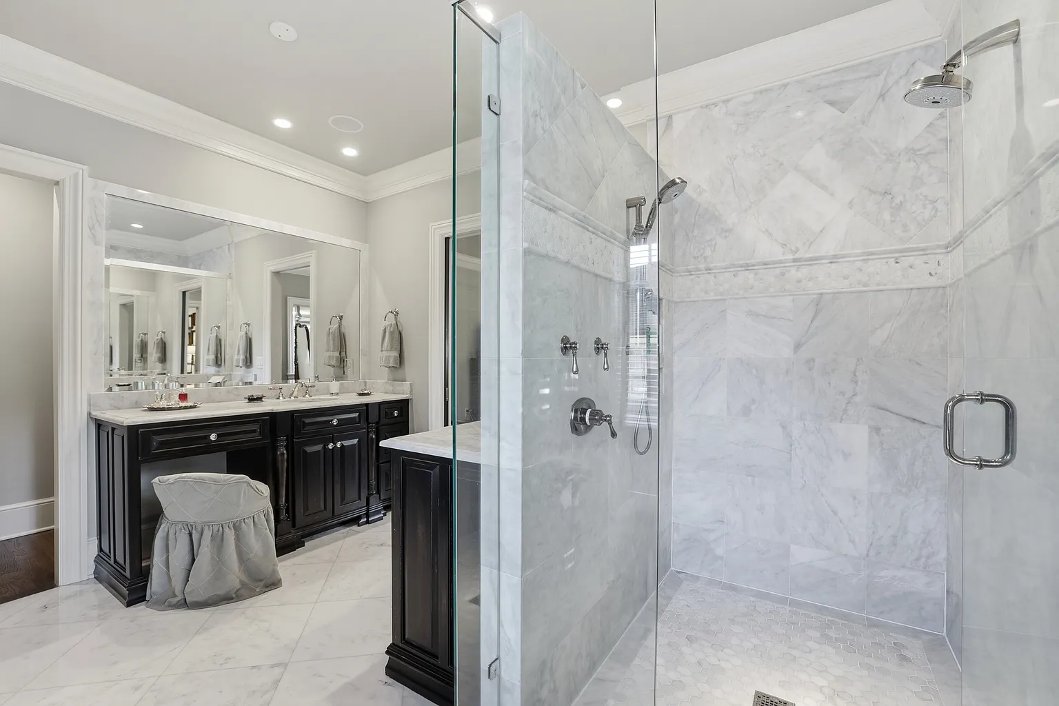 Primary bathroom with black double vanity cabinetry, marble shower tile, white-and-gray stone surfaces, frameless glass shower, hexagon mosaic shower floor, and polished chrome fixtures in Harrisburg, NC