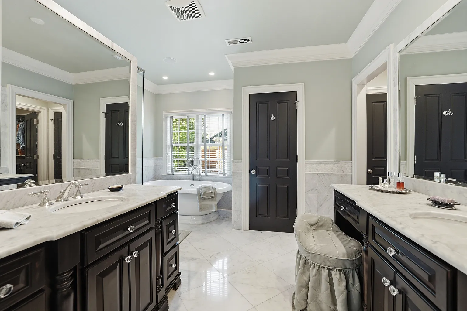 Spacious primary bathroom with two black vanities, white stone countertops, polished floor tile, freestanding bathtub, black doors, and light gray walls in Harrisburg, NC
