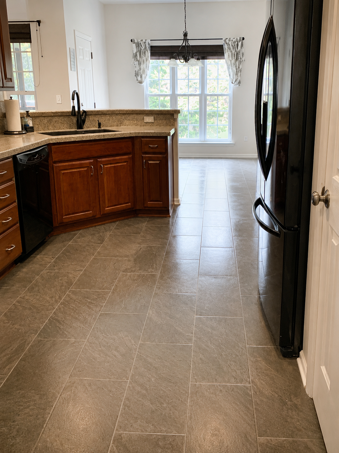 Gray rectangular tile flooring installed continuously through a residential kitchen and adjoining dining area with wood cabinetry and black appliances in Mount Holly, NC