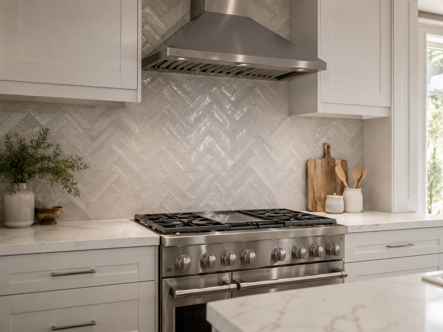 White kitchen range wall with glossy handmade-look herringbone backsplash tile, stainless steel range and hood, white shaker cabinets, and marble-look countertops in Charlotte, NC in the Ballantyne Area.