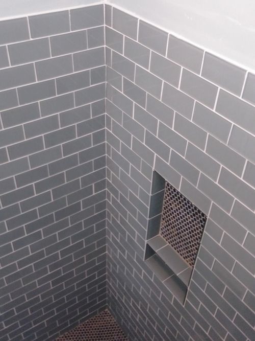 Walk-in shower with glossy blue-gray subway wall tile, contrasting white grout, dark penny-round mosaic floor, recessed niche, and glass enclosure in Indian Trail, NC
