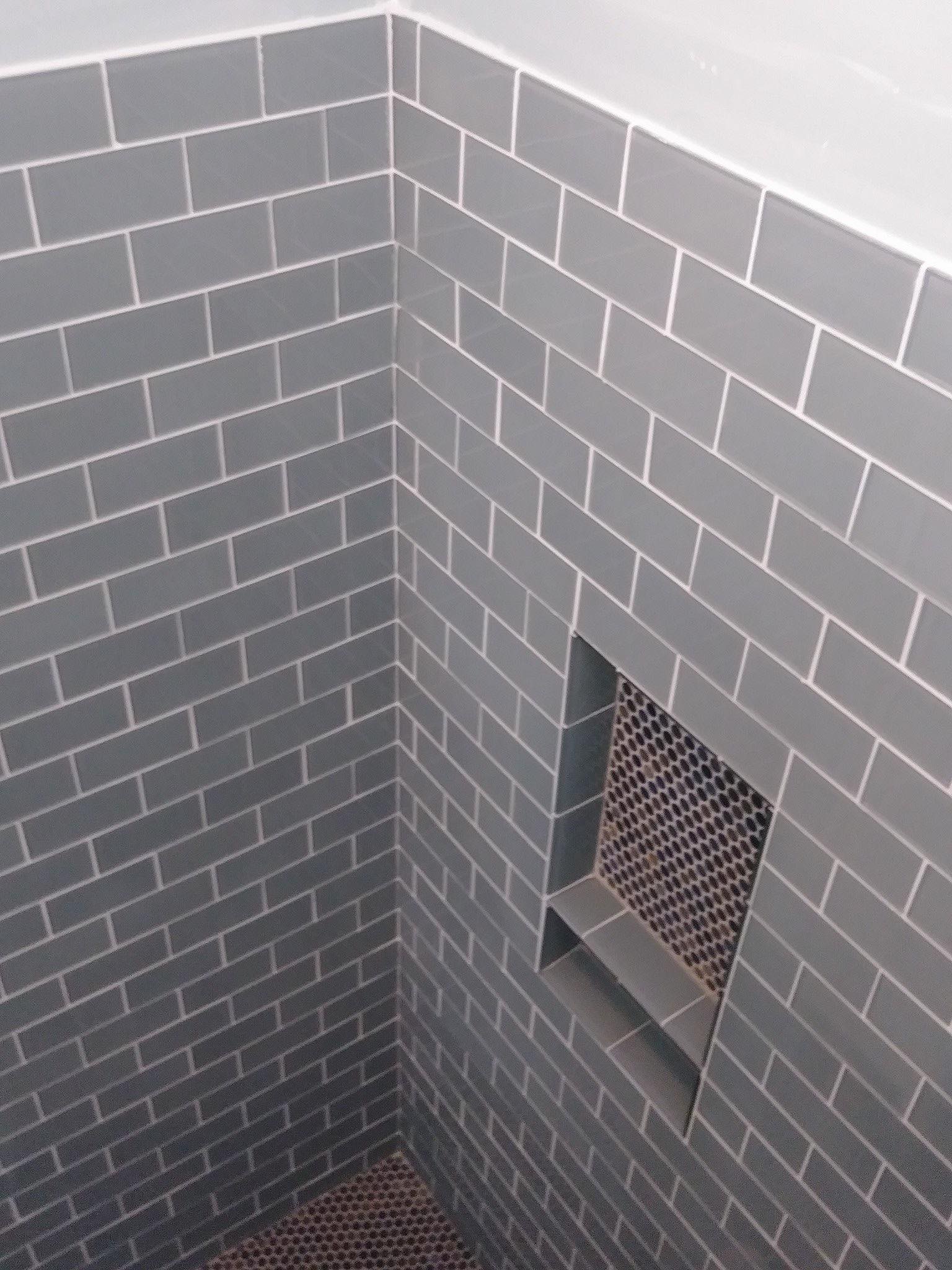 Walk-in shower with glossy blue-gray subway wall tile, contrasting white grout, dark penny-round mosaic floor, recessed niche, and glass enclosure in Indian Trail, NC