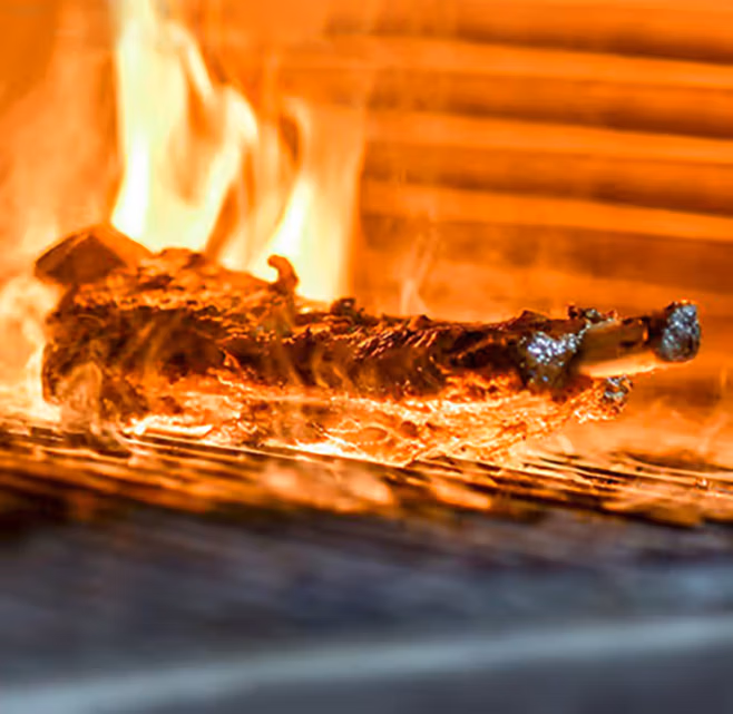 Costilla de res asándose a las brasas en el horno de DANTE Brasa y Fuego