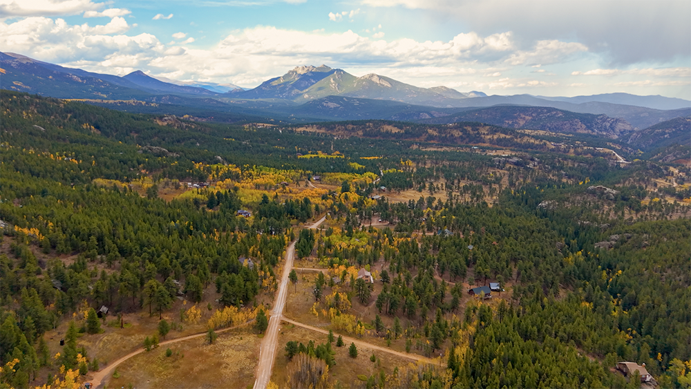 Aerial drone photo of the Allenspark neighborhood in Colorado, with mountain homes in pine and aspen forest below the peaks of Rocky Mountain National Park.