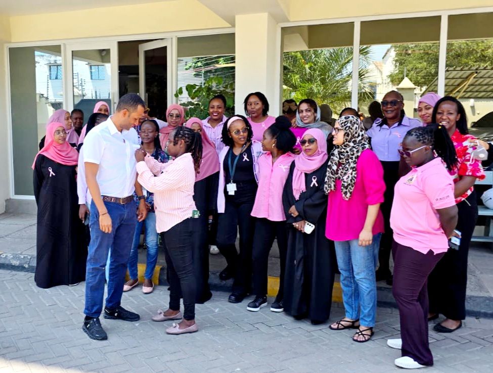 A colleague gets a pink ribbon pinned on, with the team gathered nearby