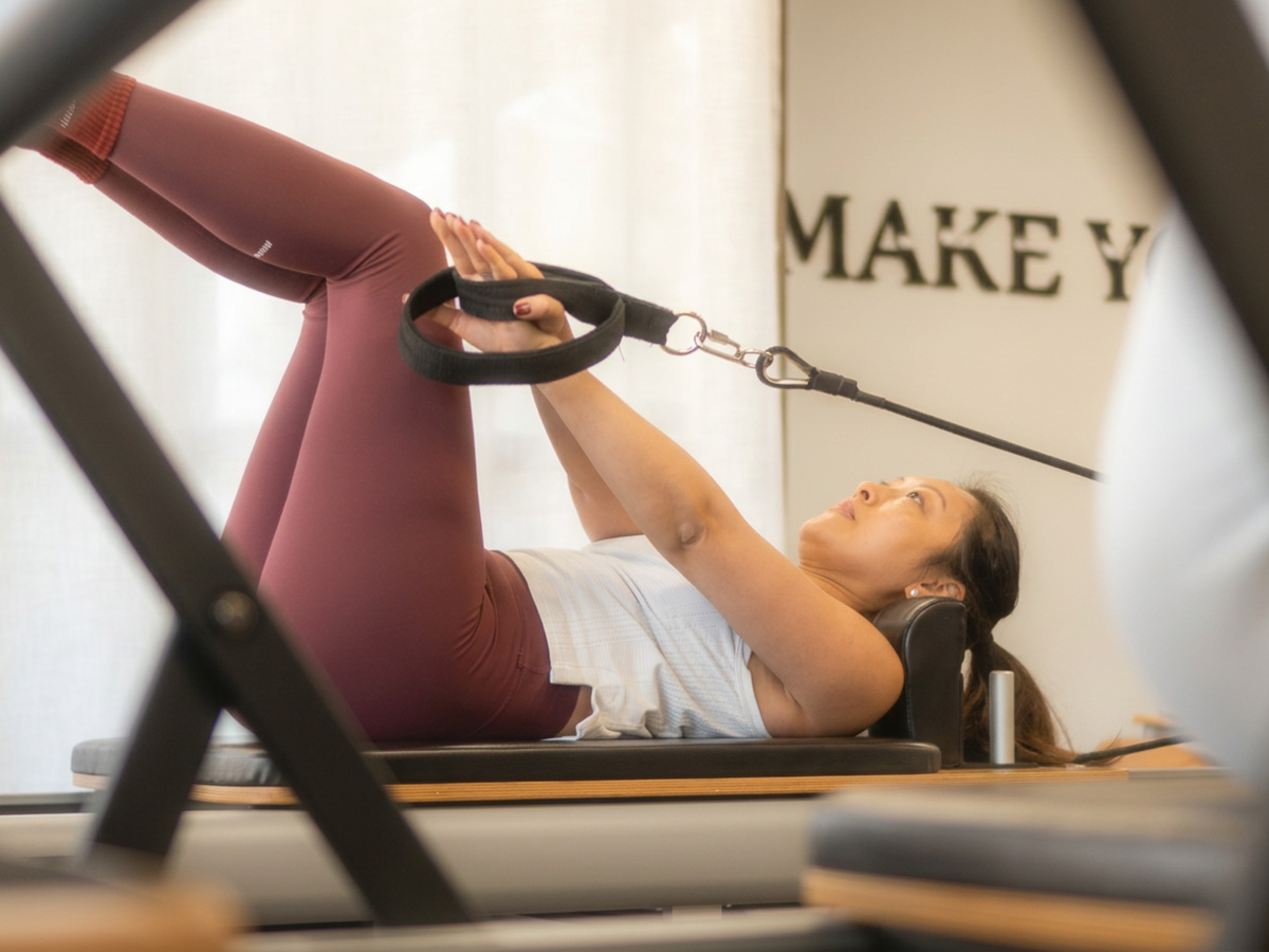Woman using resistance straps for a core exercise on a Pilates reformer