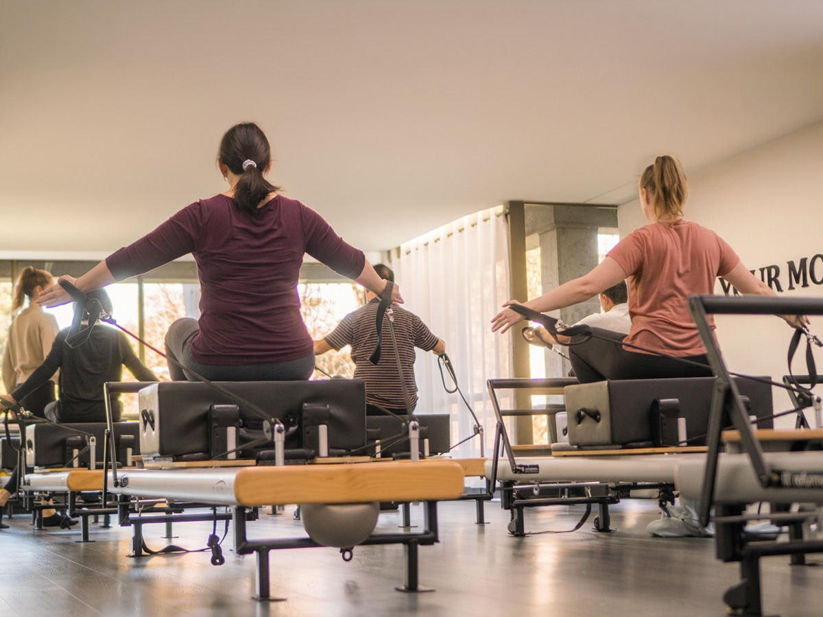 Group reformer Pilates class performing seated resistance strap exercises