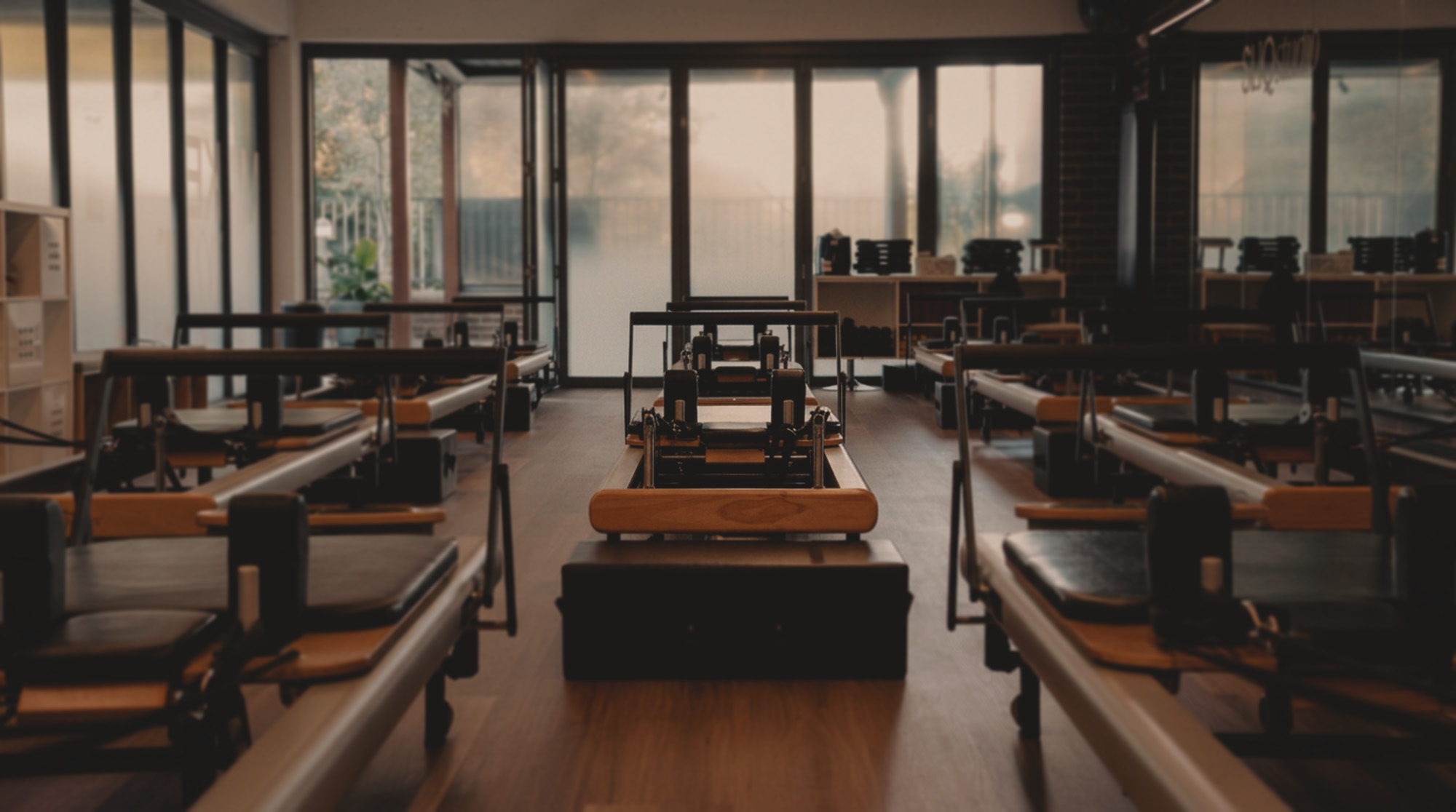 Pilates reformer machines in a studio with large windows showing trees outside.