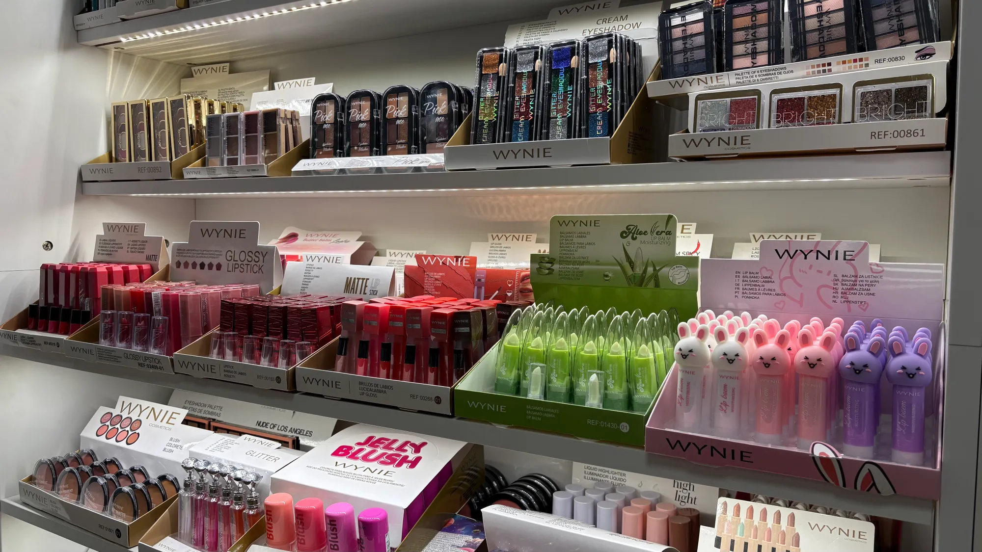 Display shelf filled with WYNIE brand cosmetics including lipsticks, lip balms, eyeshadows, and blushes.